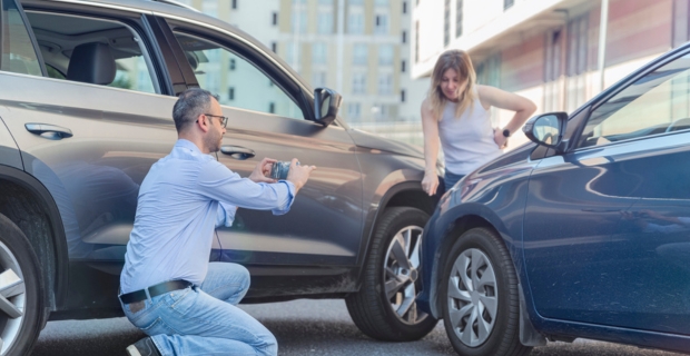 Man taking pictures of a car accident while a woman points out the damage.