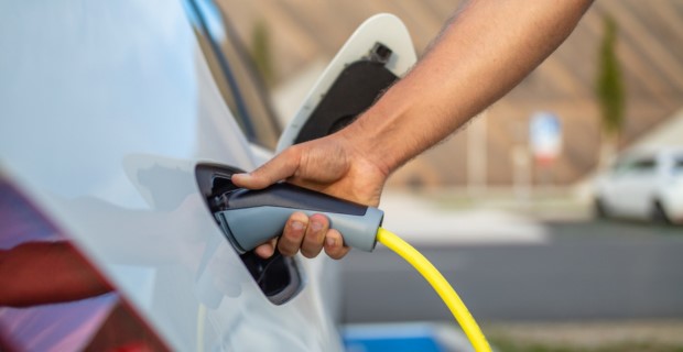 A close-up of someone attaching the charging cable for an electric vehicle to the charging port on their electric car.  