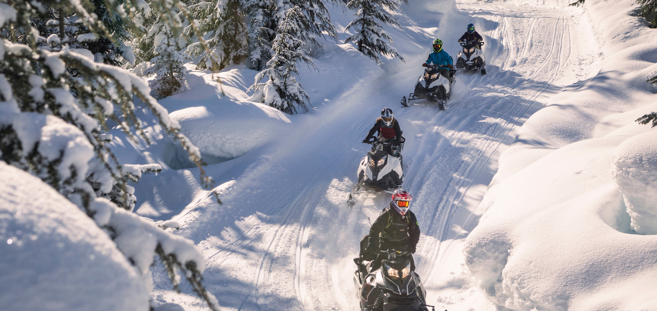 A group of people snowmobiling on a trail in the winter.