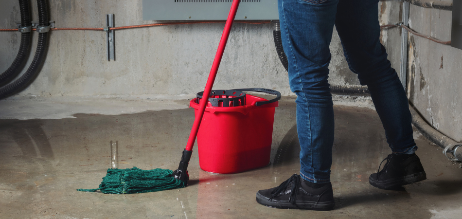 Person mopping standing water in a flooded basement, illustrating the importance of coverage for water damage.