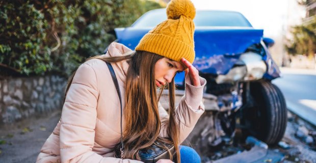 Frustrated woman crouches next to wrecked car after a car collision