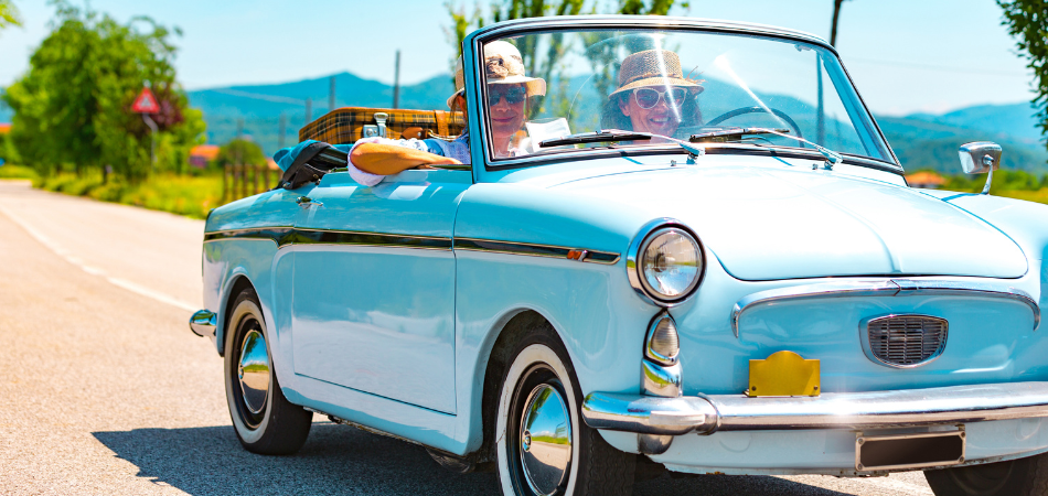 A couple driving in a Robin blue convertible collector car on a beautiful sunny day. The wind gently tousles their hair as they enjoy the open road and the warmth of the sun. The image captures the carefree spirit of a leisurely drive in a classic car, evoking a sense of nostalgia and the joy of summertime adventures.