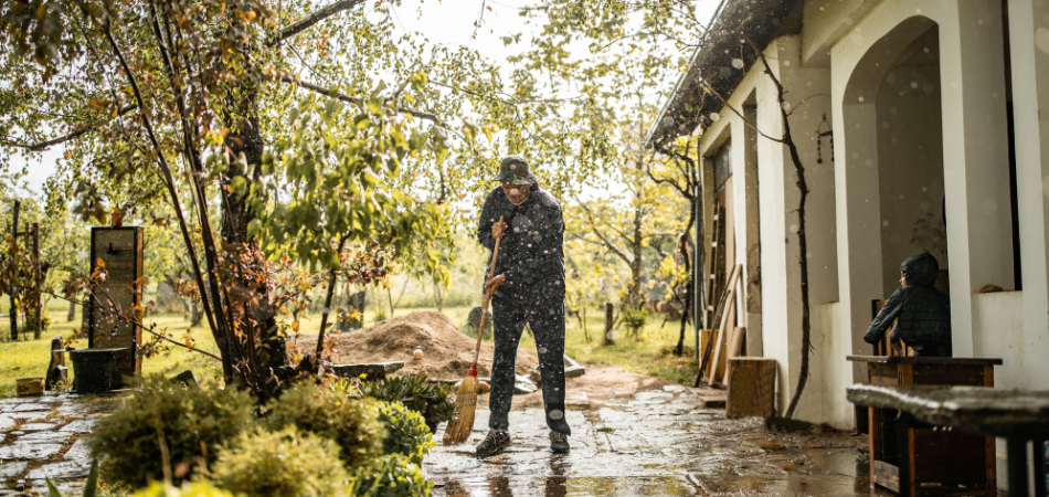 A homeowner in their flooded backyard sweeping water away from the house on a rainy day.