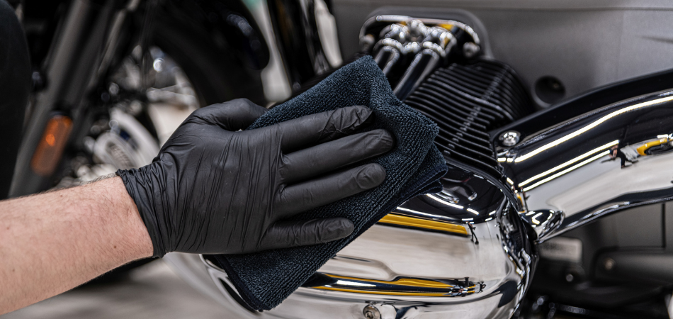 Gloved hand cleaning motorcycle engine during motorcycle winter storage preparation.  
