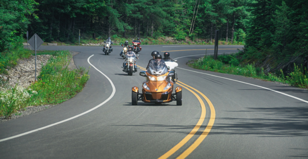 In La Mauricie National Park, motorcyclists drive in a group on a road by the park. 