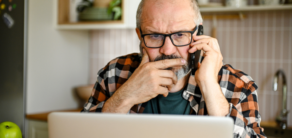 Person using a laptop and phone to verify a potential AI scam at home.