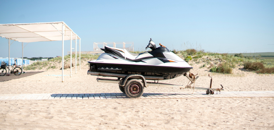A personal watercraft is on a trailer sitting on a walkway near a beach.   