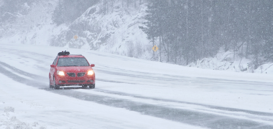 A red vehicle driving on a snowy road practicing winter road safety.