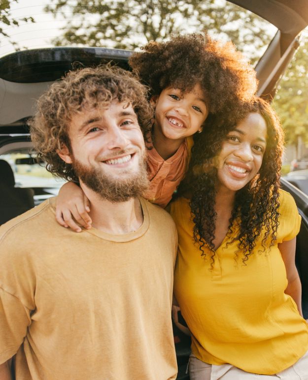 A family poses at under the open hatch of their car before they head out on a road trip.