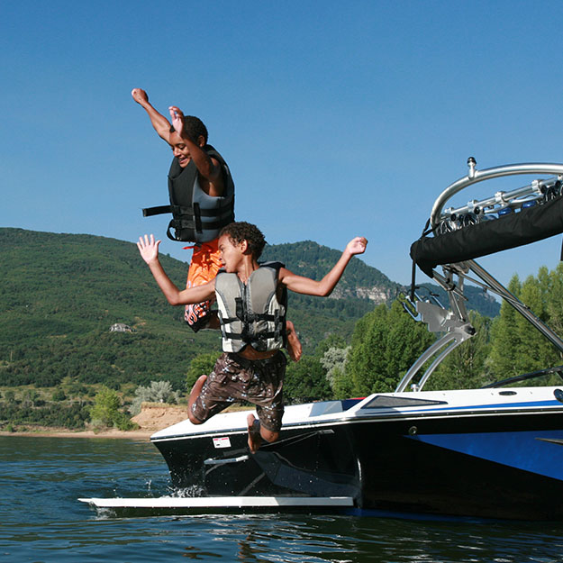 Two young boys joyfully jumping off the back of a boat