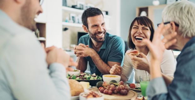 A group of friends laughing and talking around the dinner table.