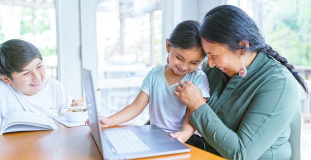 A parent sitting at the kitchen table with her kids, laughing and smiling. 