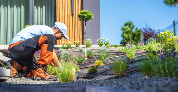 A man is seen doing landscaping to improve the drainage around a home to prevent long-term damage 