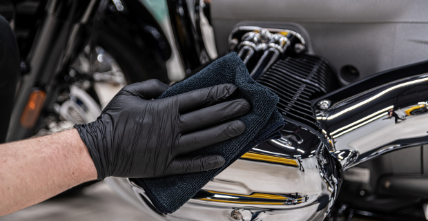 Gloved hand cleaning motorcycle engine during motorcycle winter storage preparation.  