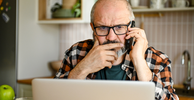 Person using a laptop and phone to verify a potential AI scam at home.   