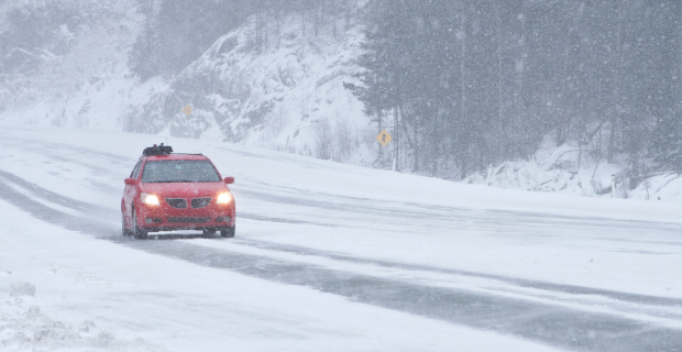 A red vehicle driving on a snowy road practicing winter road safety.