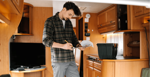 A man standing in his RV with a clipboard working through his spring RV maintenance checklist for the coming season.