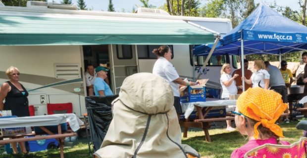 FQCC: People gather outdoors beside an RV and tents during a community event with tables and supplies set up.