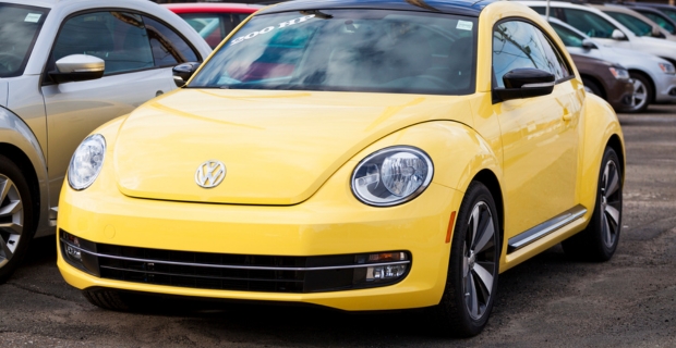 Front and side profile of a yellow Volkswagen Beetle parked at a dealership. 