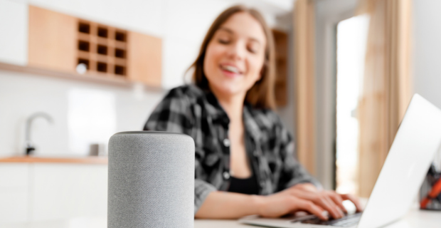 Young girl using her laptop in the kitchen of her home while speaking to a smart home device.