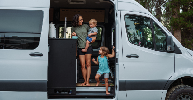 A woman standing in her motorhome holding a child and preparing food for them.