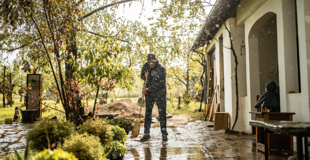 A homeowner in their flooded backyard sweeping water away from the house on a rainy day.